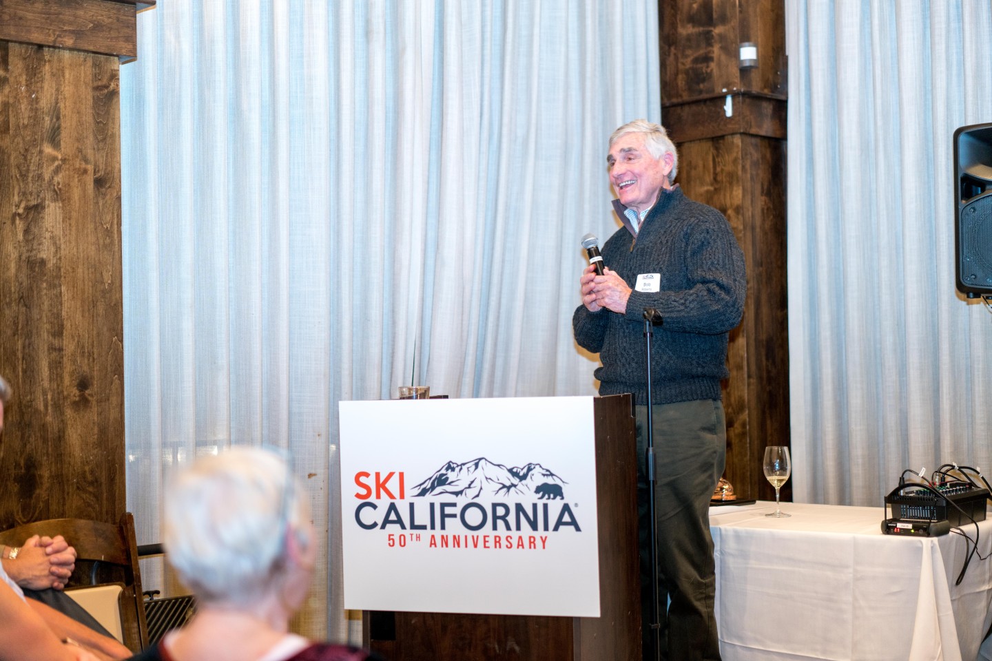 Bob Roberts speaking at a podium with a Ski California logo, indoors.